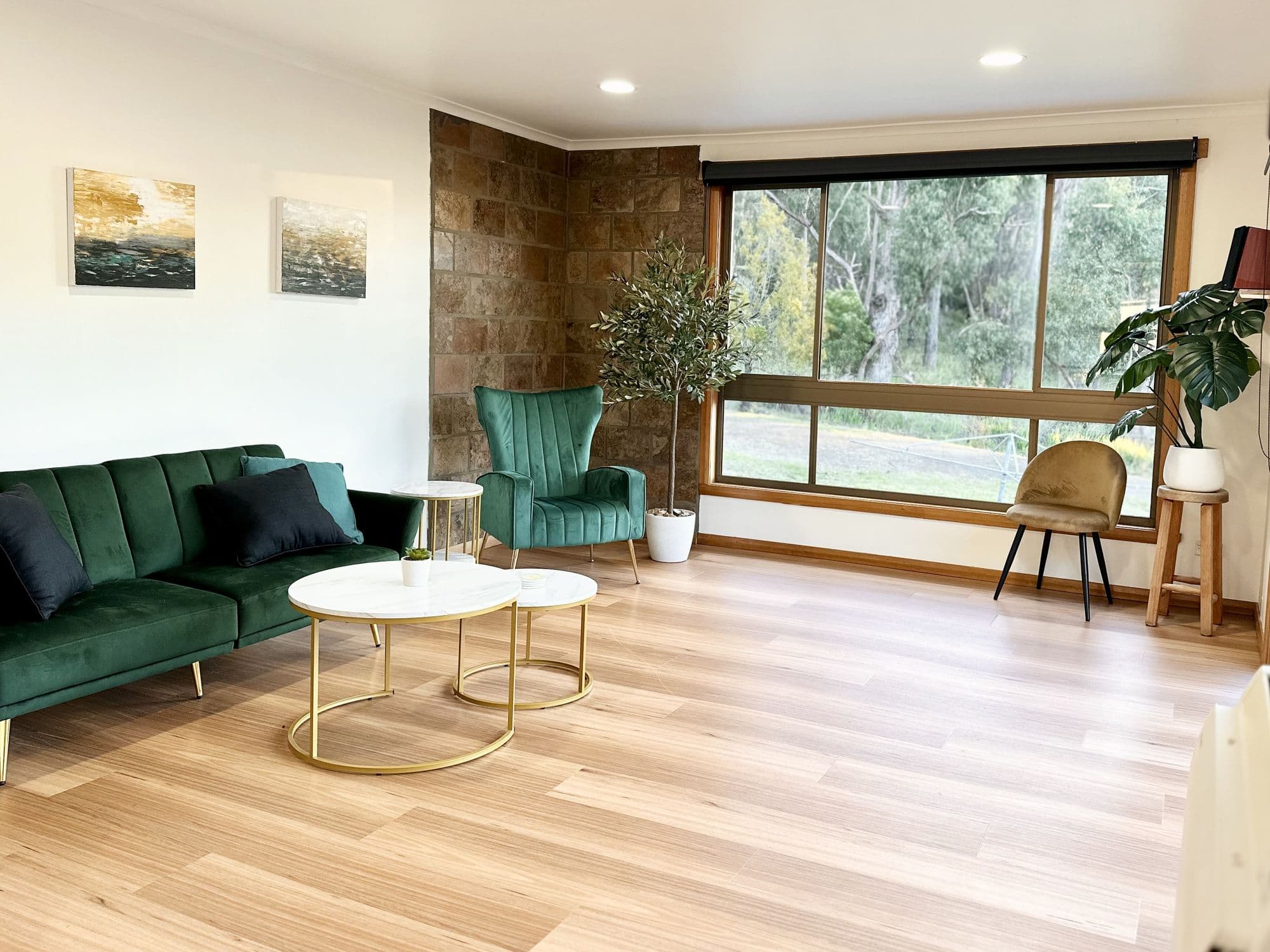 LunaStay living room — green velvet sofa, slate feature wall, picture window to the bush
